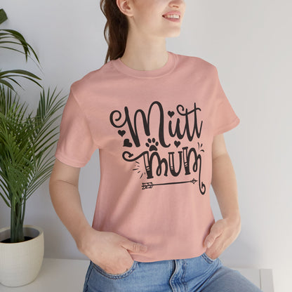 Person wearing a pink t-shirt with 'Mutt Mum' text, standing indoors next to a plant.
