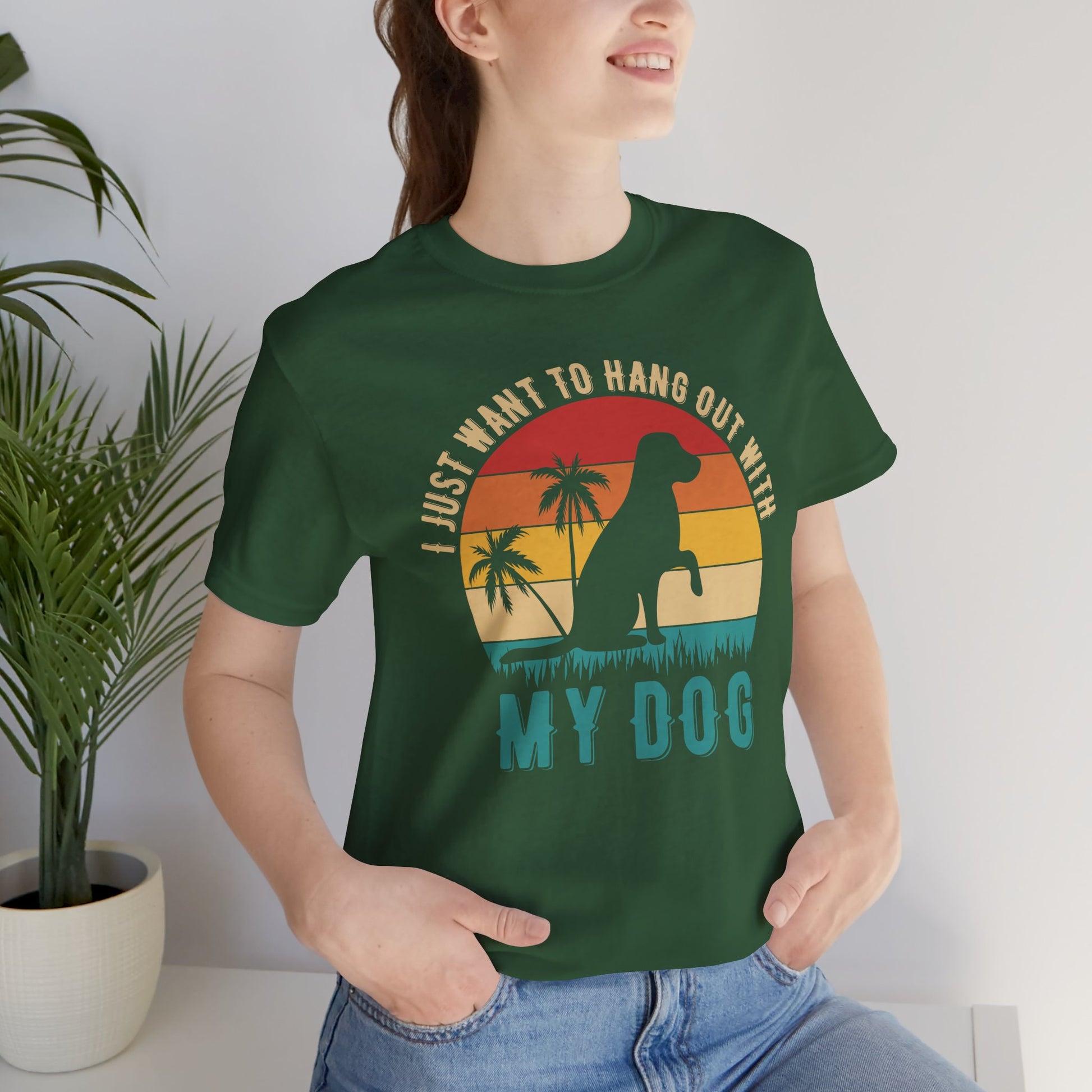 Person wearing a green t-shirt with a dog graphic and text, standing indoors next to a plant.
