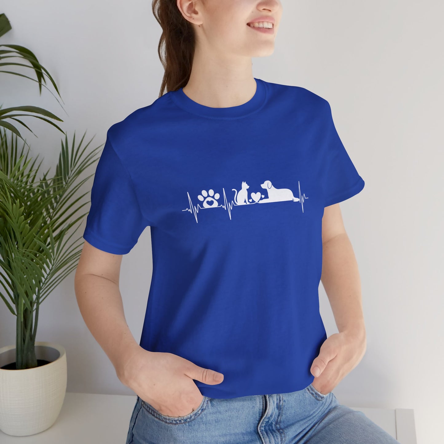 Person wearing a blue t-shirt with text, standing indoors next to a plant.