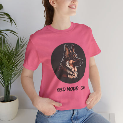 Person wearing a pink t-shirt with a dog graphic and text, standing indoors next to a plant.