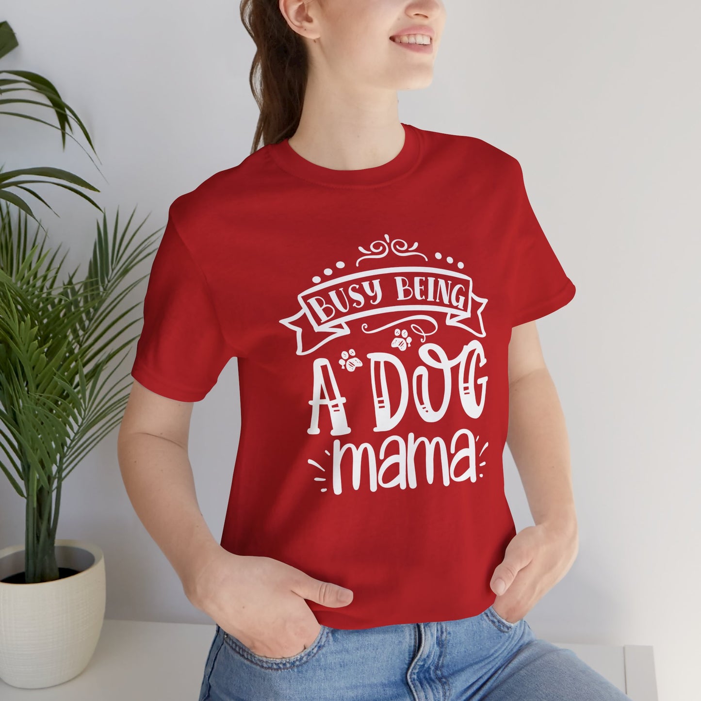 Person wearing a red t-shirt with 'Busy Being A Dog Mama' text, standing indoors.