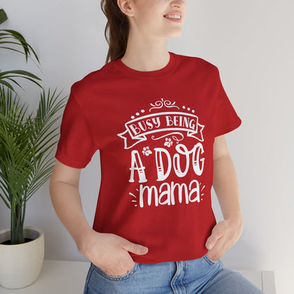 Person wearing a red t-shirt with 'Busy Being A Dog Mama' text, standing indoors.