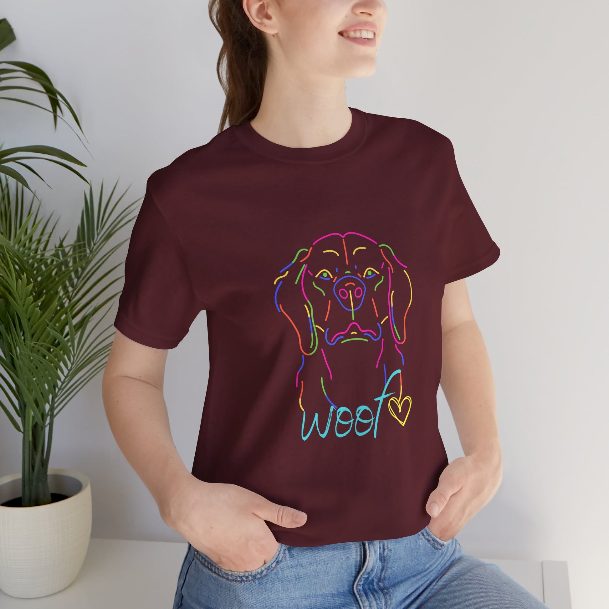 Person wearing a maroon t-shirt with a colorful dog illustration and 'woof' text, standing indoors.