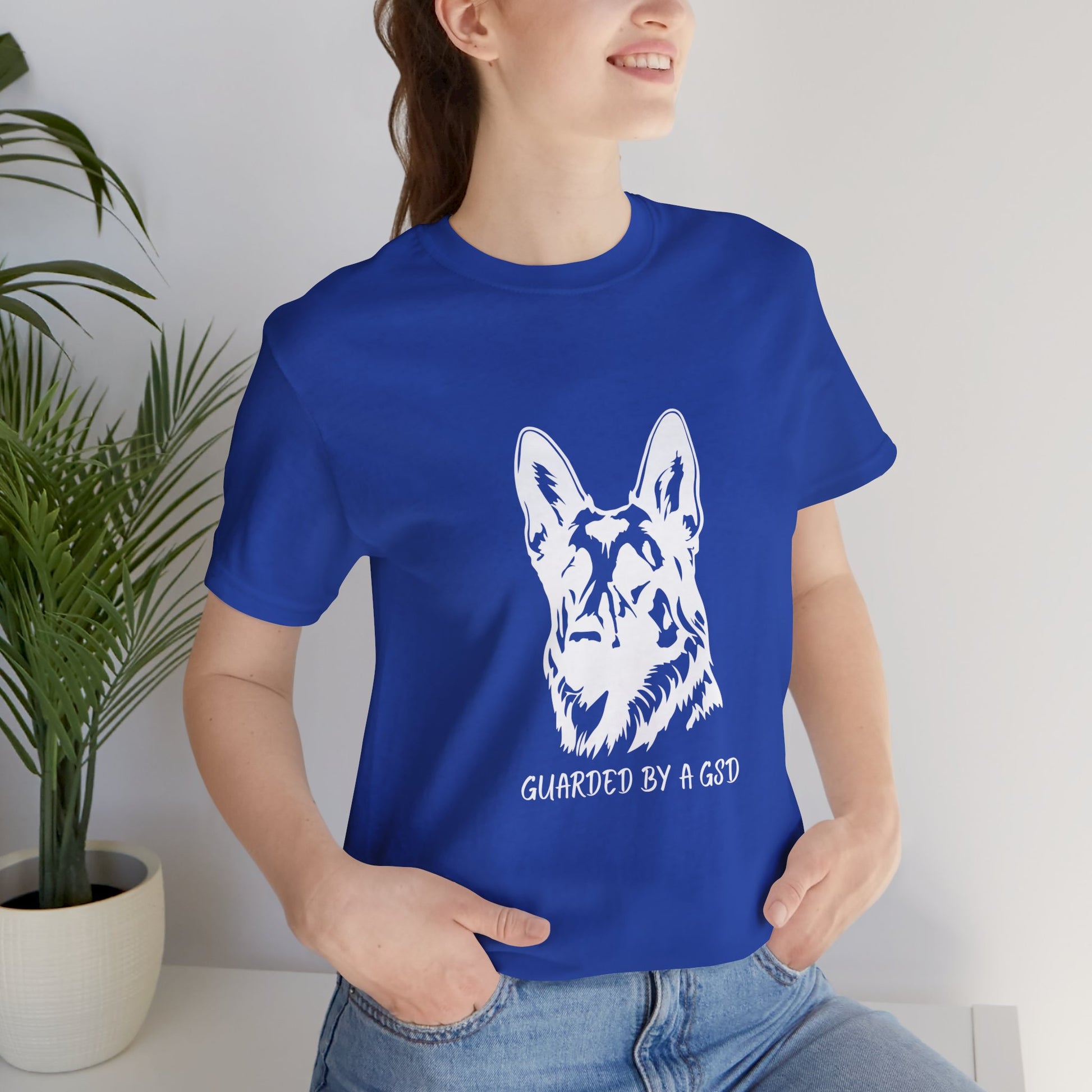 Person wearing a blue t-shirt with a white dog graphic and text, standing indoors.