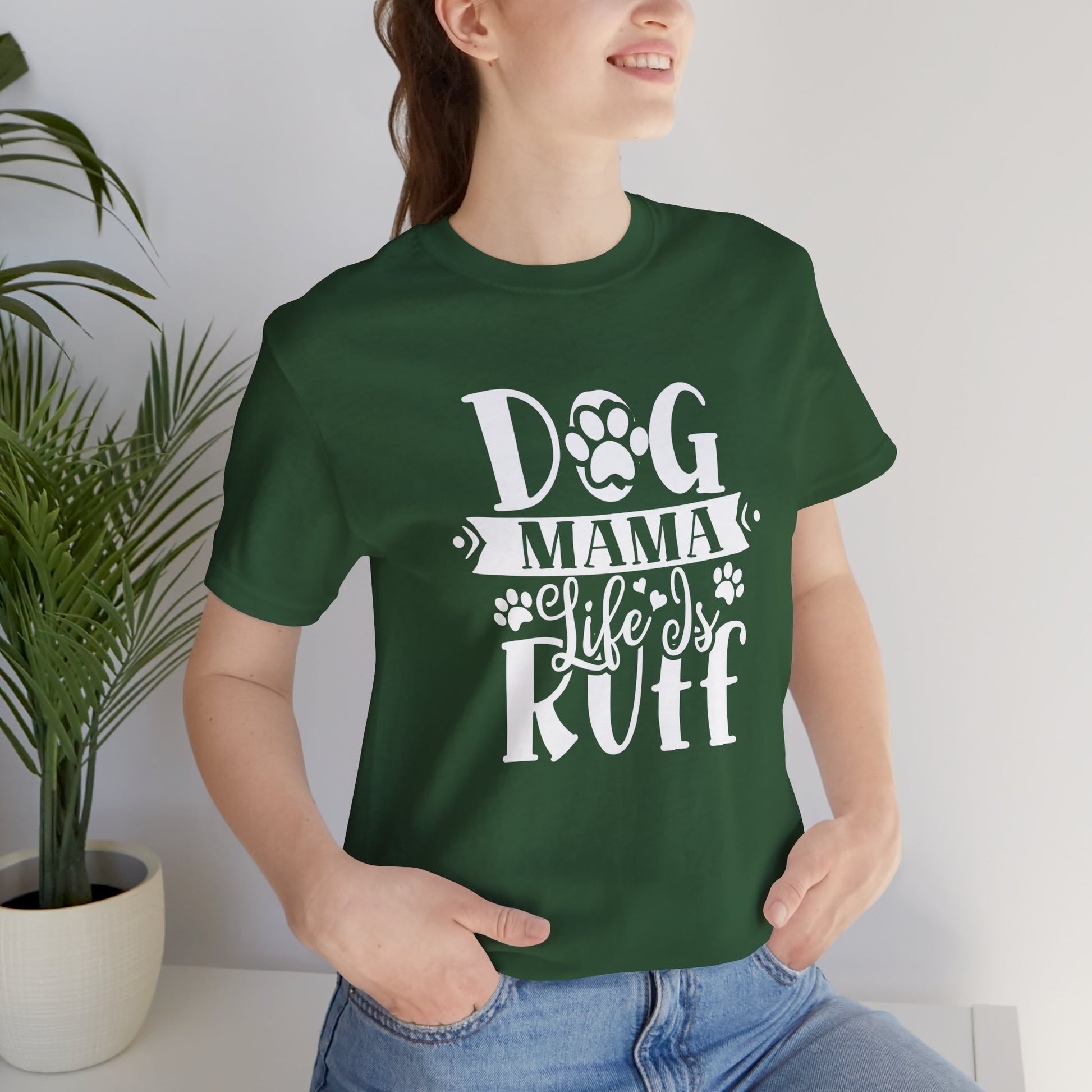 Person wearing a green t-shirt with 'Dog Mama Life is Ruff' text, standing indoors next to a plant.
